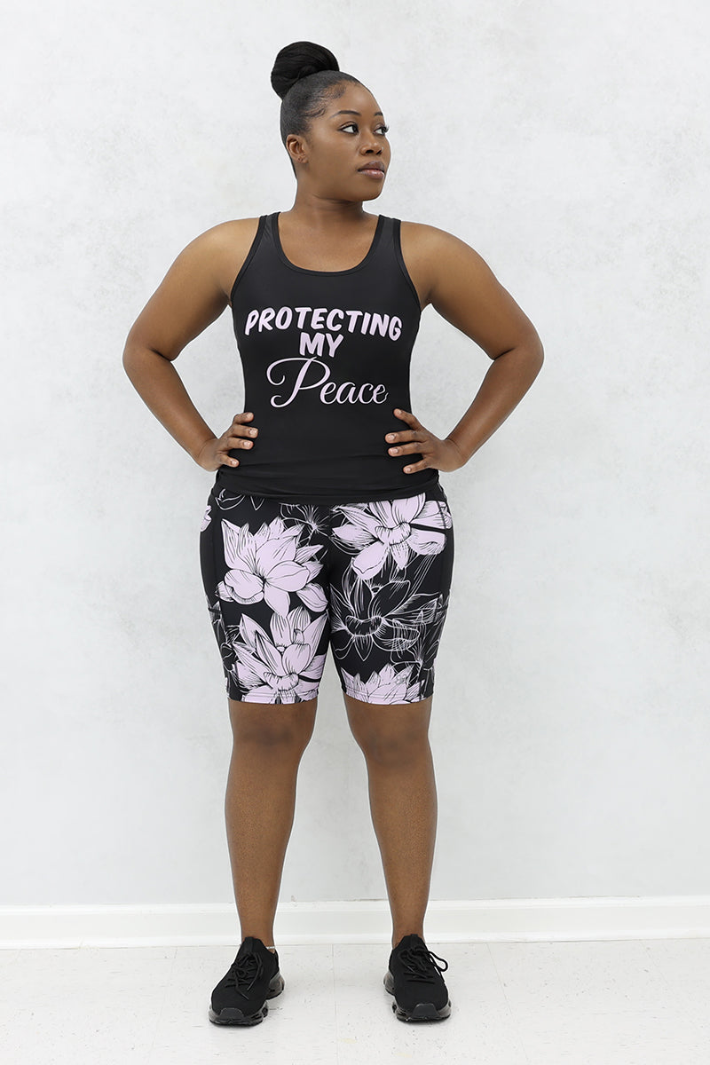 a woman wearing a black 
tank top with 'Protecting My Peace,' printed on the front 
paired with black and lavender floral printed shorts