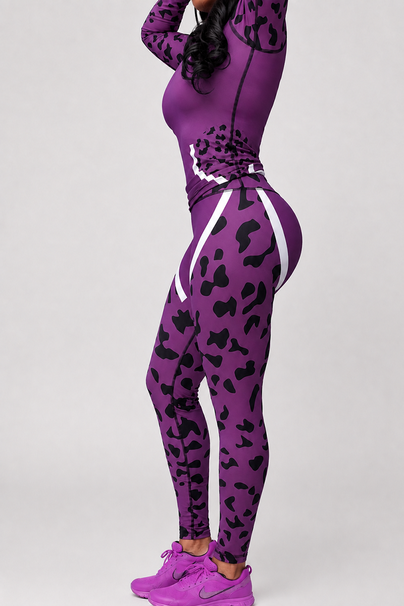 A person poses in the Purple Leopard Half-Zip Pullover, an athletic jacket made from a polyester spandex blend for comfort and flexibility. The pullover features a purple animal-print design with black spots and white stripes, paired with matching sneakers. The background is plain and light-colored, and the person’s face is not visible.