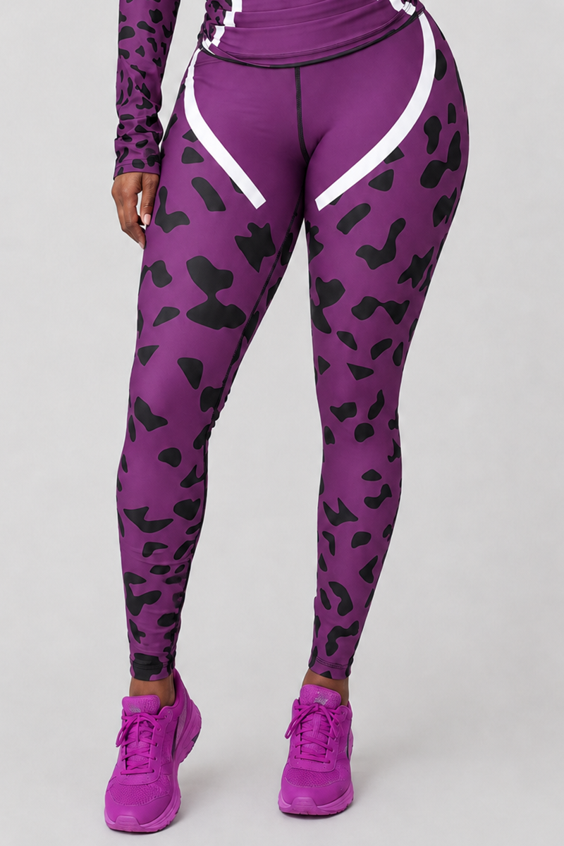 A person is wearing Purple Leopard Tights in a purple-black colorway, featuring a body-contouring fit that accentuates their silhouette. The tights display black abstract spots with white accents and are paired with a matching long-sleeve top. Bright purple athletic shoes complete the look against a plain light gray background.
