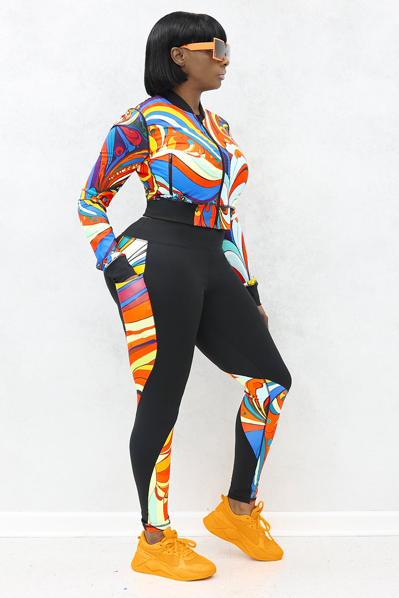 A woman wearing a multi-colored Slit Back Long Sleeve top with vibrant swirl patterns, featuring a snug fit and stylish design ideal for workouts or casual outings.