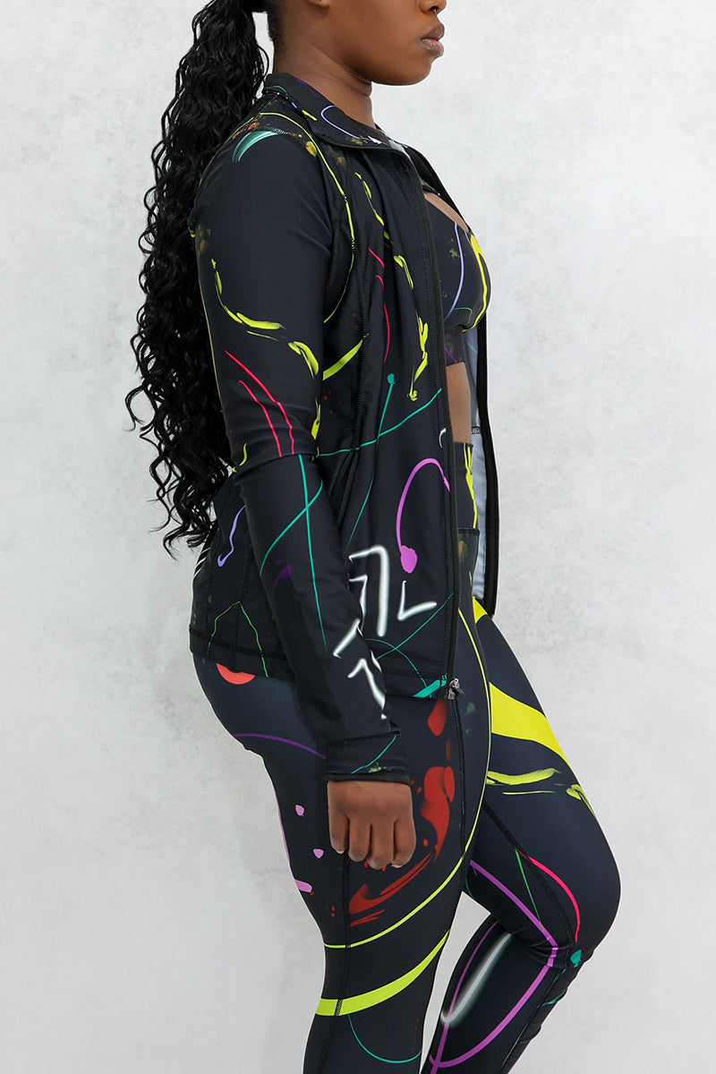 A woman wearing a multi-colored Space Girl Jacket with a glow effect, featuring thumbholes and the Brick-Built logo, perfect for stylish workouts or casual outings.