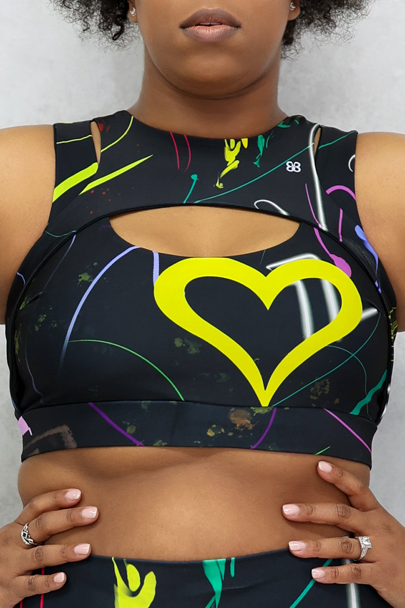 A woman wearing a multi-colored Space Girl Sports Bra with a glow-like design, featuring a cut-out design on the front and back, and heart-shaped detail, perfect for active workouts.