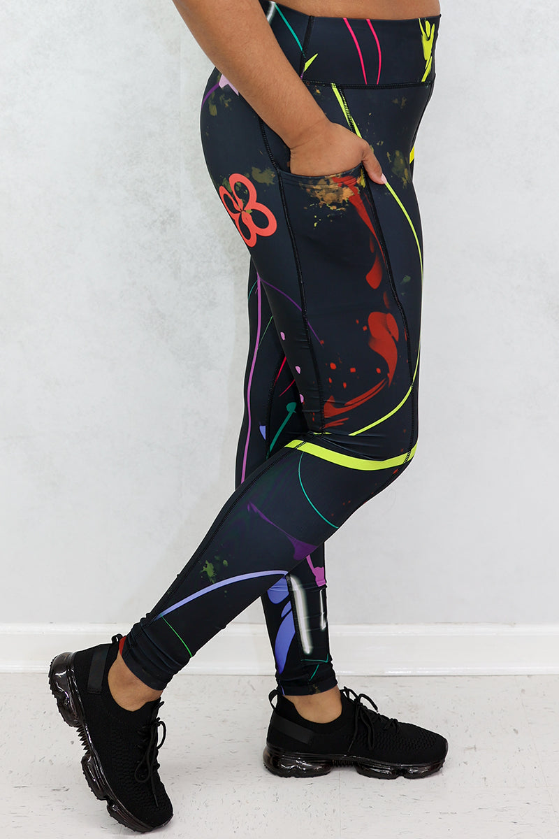 A woman wearing multi-colored Space Girl Tights with a glow effect, featuring the Brick-Built logo, pockets, and a zippered pocket on the back of the waistband, perfect for stylish workouts.