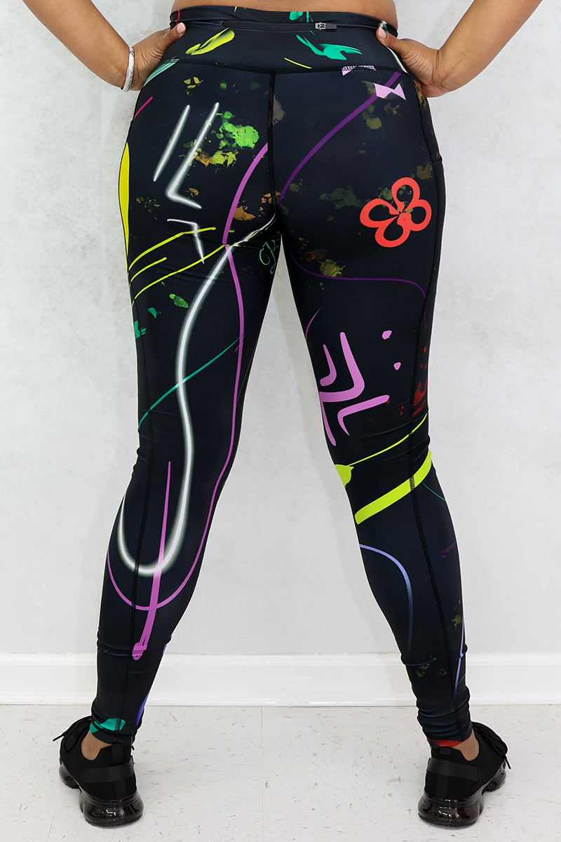 A woman wearing multi-colored Space Girl Tights with a glow effect, featuring the Brick-Built logo, pockets, and a zippered pocket on the back of the waistband, perfect for stylish workouts.