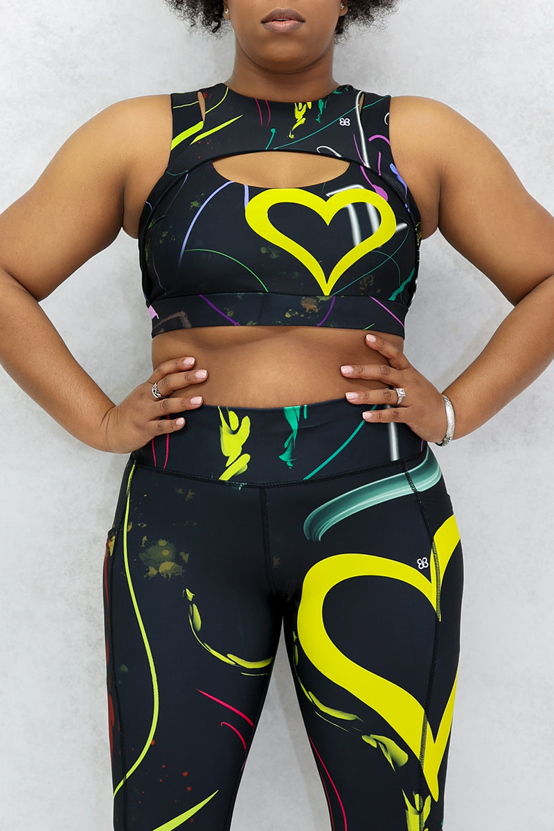 A woman wearing a multi-colored Space Girl Sports Bra with a glow-like design, featuring a cut-out design on the front and back, and heart-shaped detail, perfect for active workouts.