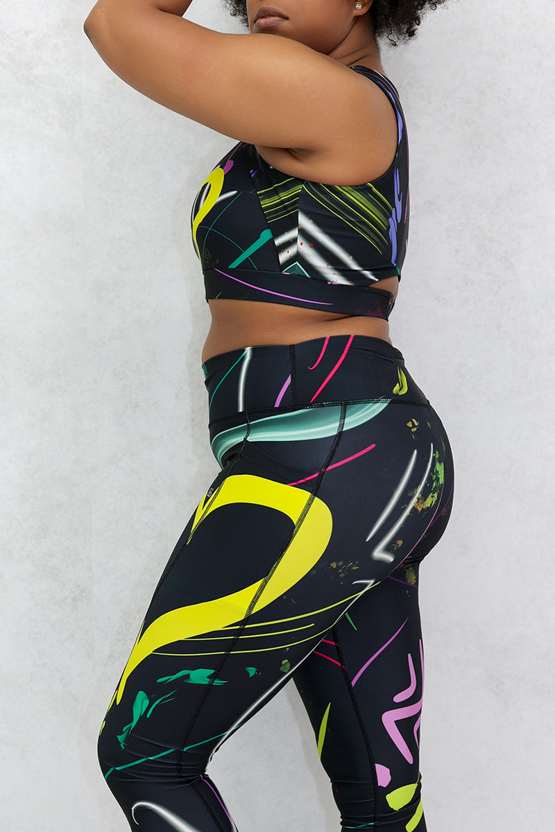 A woman wearing multi-colored Space Girl Tights with a glow effect, featuring the Brick-Built logo, pockets, and a zippered pocket on the back of the waistband, perfect for stylish workouts.