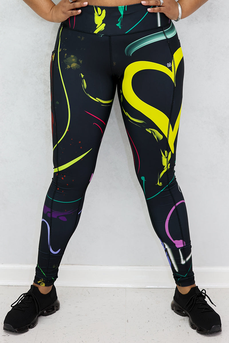 A woman wearing multi-colored Space Girl Tights with a glow effect, featuring the Brick-Built logo, pockets, and a zippered pocket on the back of the waistband, perfect for stylish workouts.