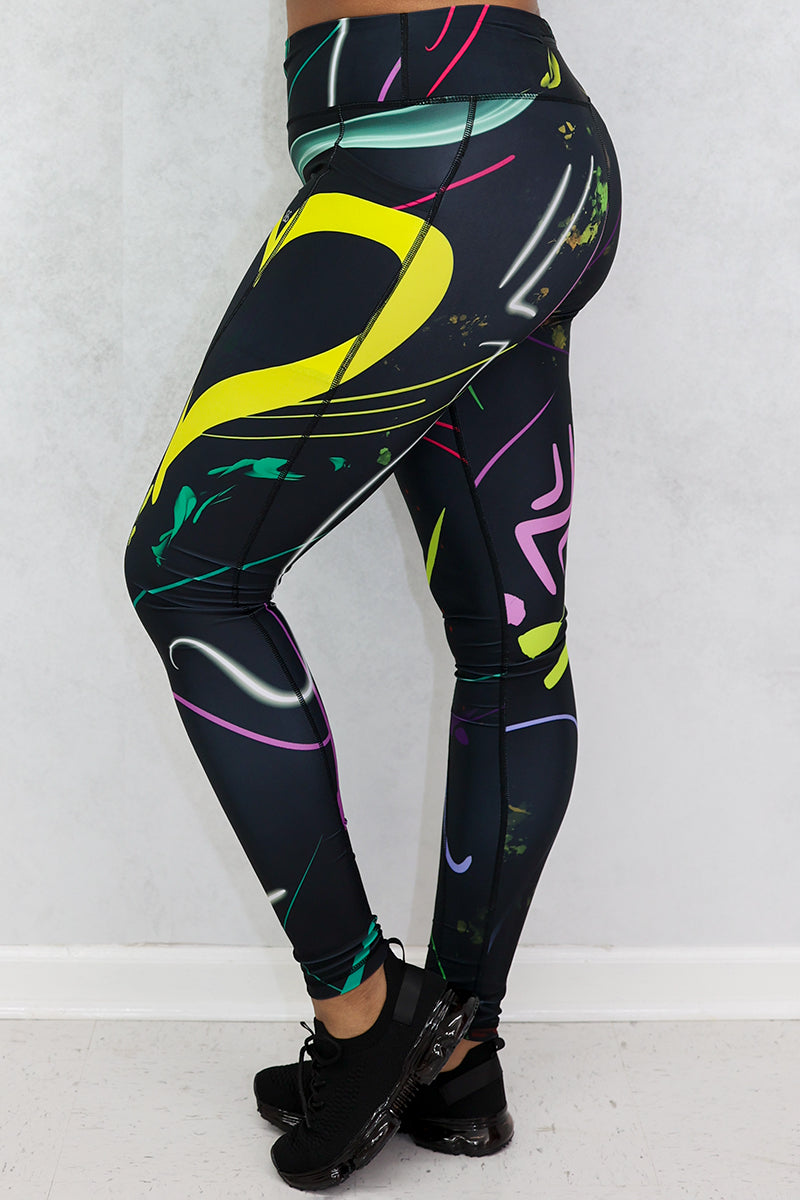 A woman wearing multi-colored Space Girl Tights with a glow effect, featuring the Brick-Built logo, pockets, and a zippered pocket on the back of the waistband, perfect for stylish workouts.