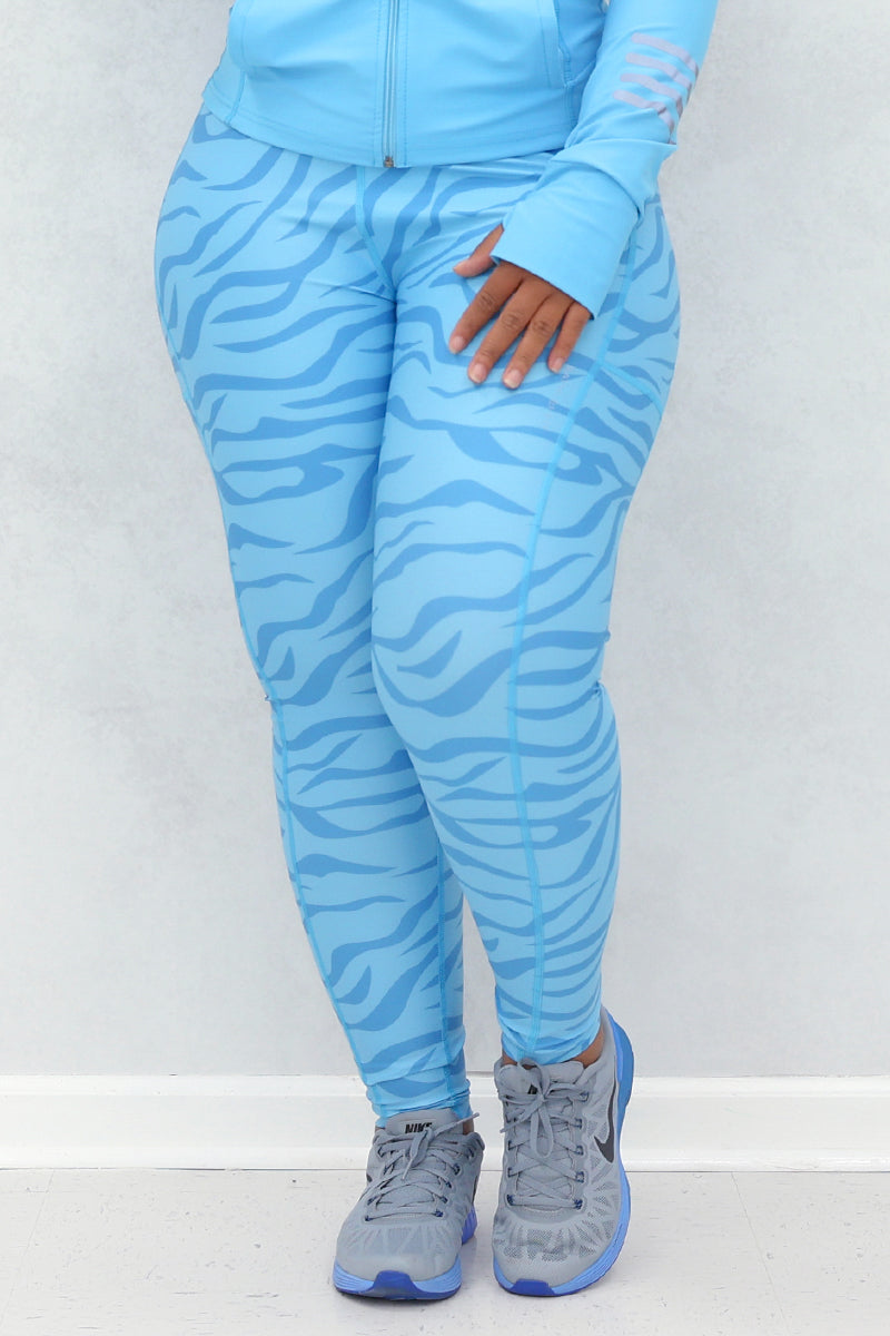 A woman wearing a light blue active wear with zebra print detailing on the leggings and sleeves, posing against a neutral background.