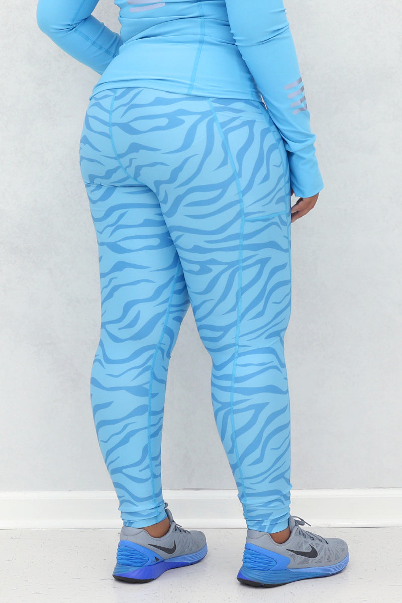 A woman wearing a light blue active wear with zebra print detailing on the leggings and sleeves, posing against a neutral background.