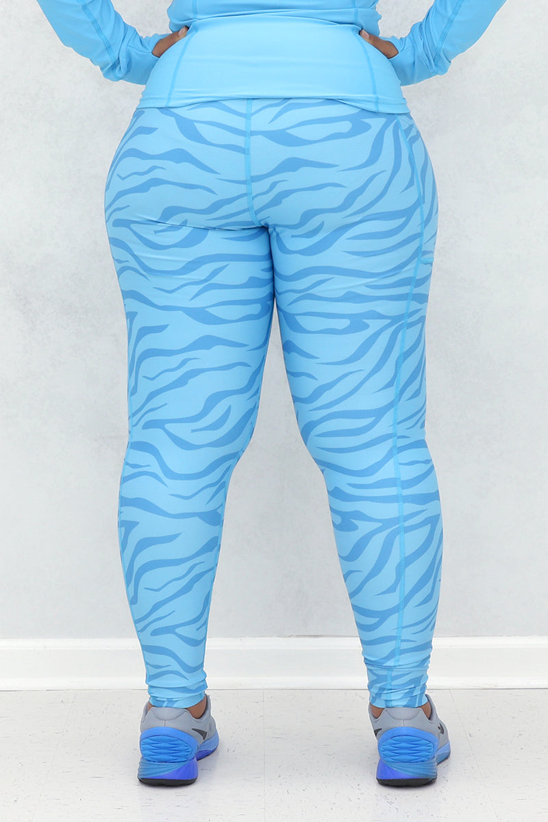 A woman wearing a light blue active wear with zebra print detailing on the leggings and sleeves, posing against a neutral background.