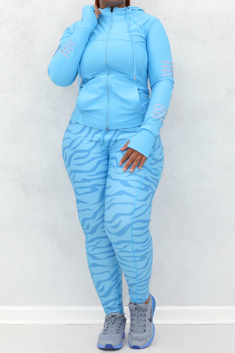 A woman wearing a light blue active wear with zebra print detailing on the leggings and sleeves, posing against a neutral background.