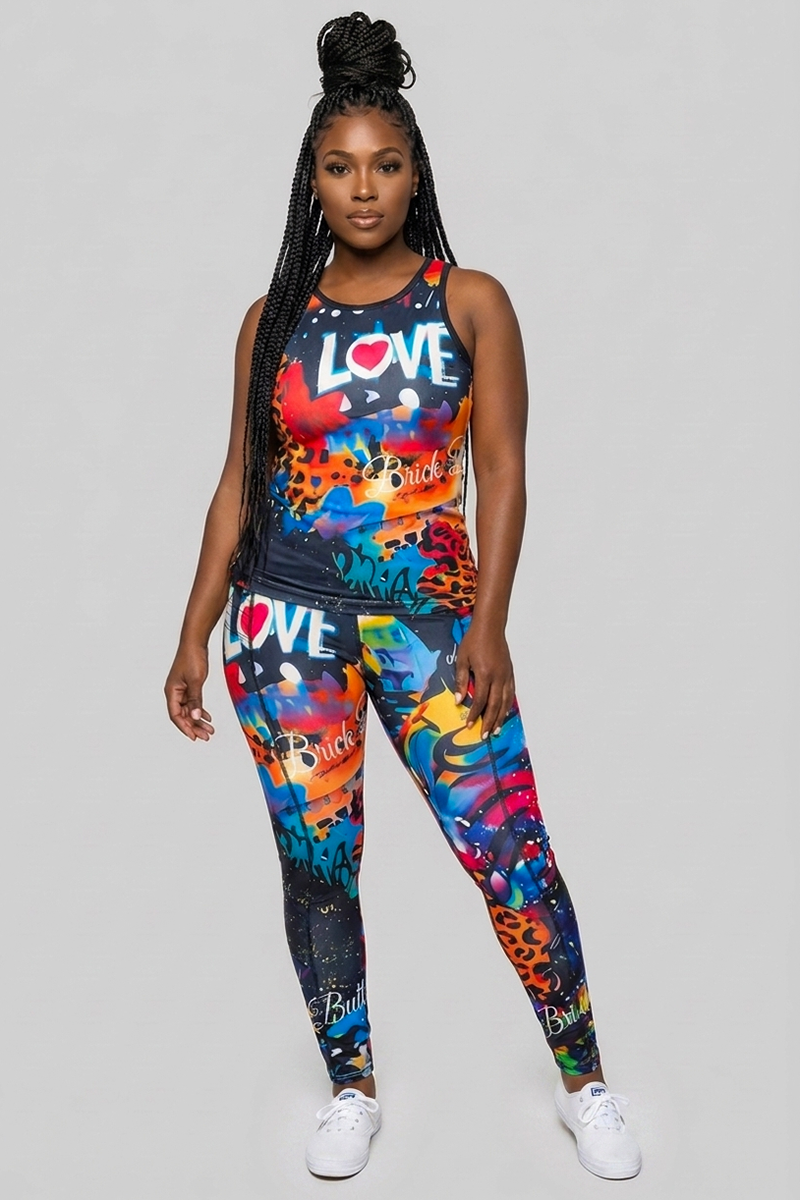 A woman stands facing forward, wearing the Art Code Tank Top—a colorful, lightweight racerback tank featuring the word LOVE and graffiti-style designs—paired with matching leggings and white sneakers. She has long braided hair and a neutral expression.