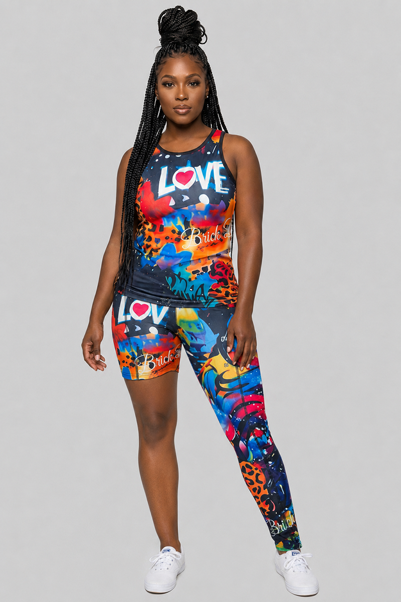 A woman stands facing forward, wearing a colorful matching tank top and the Art Code One-Legged Tights, which feature a bold “LOVE” print at the waistband. Made from a polyester-spandex blend, these tights offer 4-way stretch for comfort and flexibility. She has long braided hair and completes her look with white sneakers against a plain gray background.