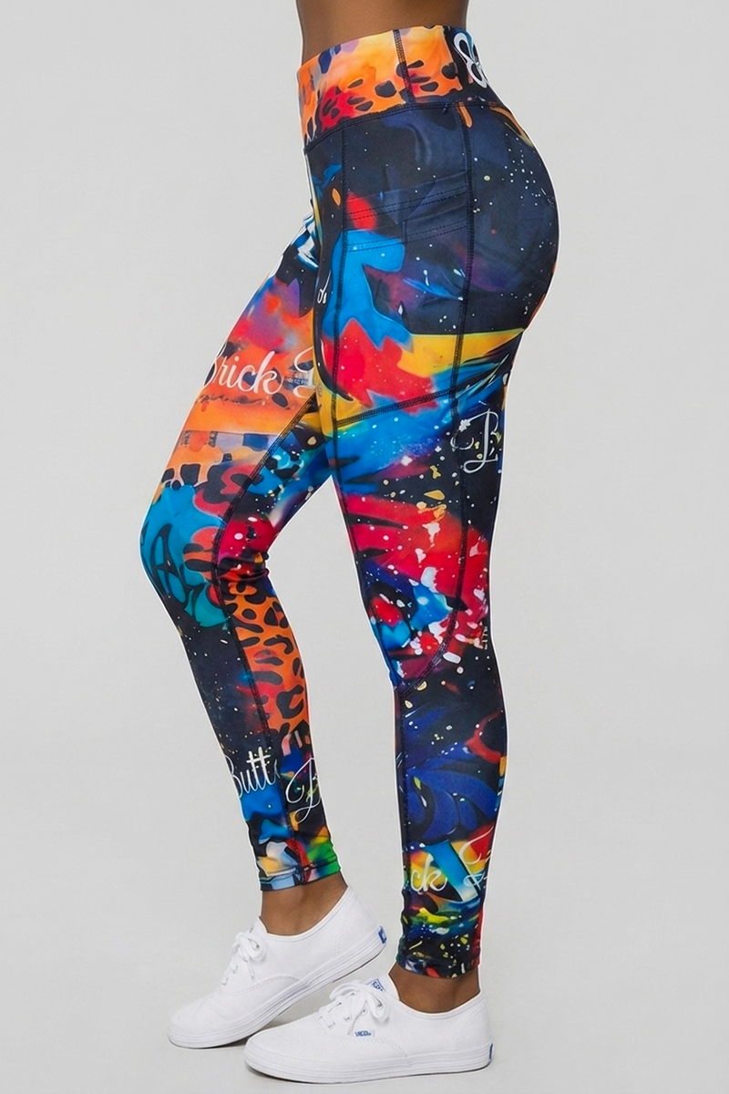 A person wearing Art Code Tights—colorful, graffiti-patterned polyester spandex athletic tights with abstract designs in red, blue, orange, and yellow—and white sneakers stands against a plain light gray background.