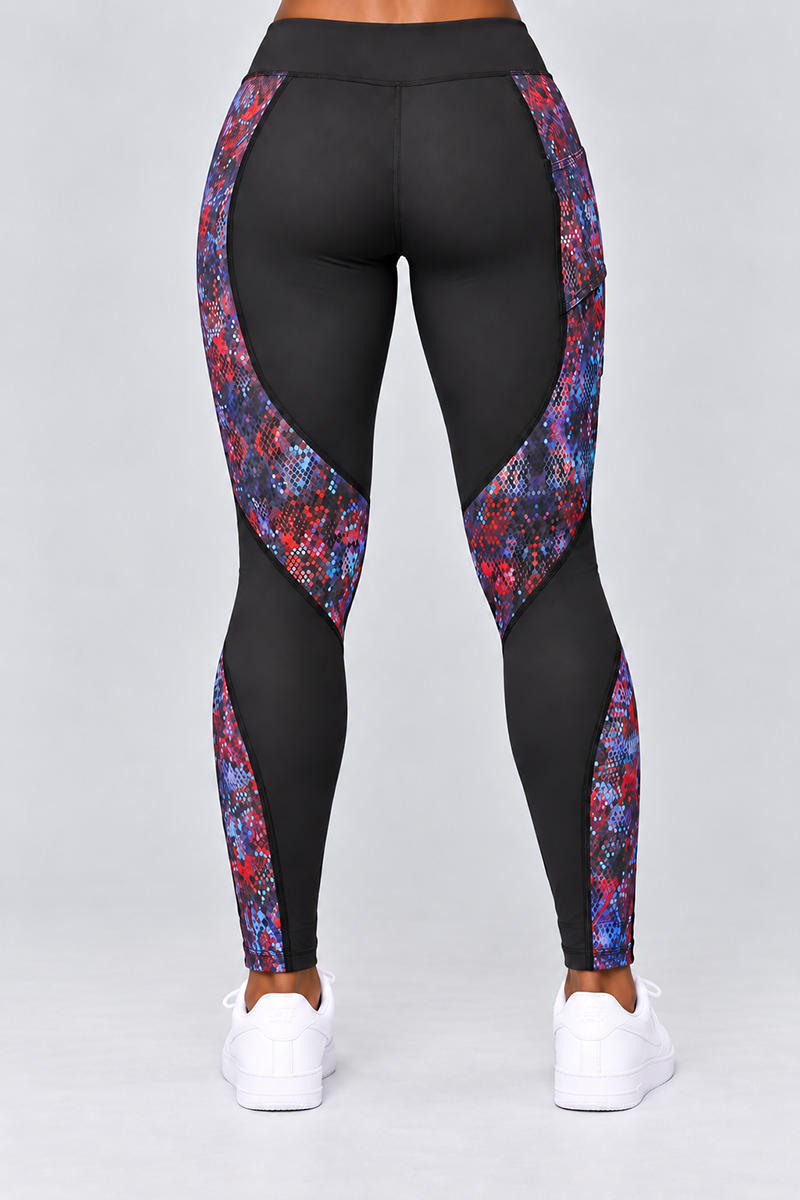 A person is standing facing away from the camera, wearing Kario Tights in Multi, featuring black body contouring panels with red, blue, and purple patterns and paired with white sneakers. Crafted from a polyester spandex blend for 4-way stretch, these leggings stand out against the plain light gray background.