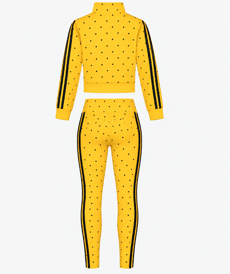 A back view of the Spotlight Tights (SAMPLE SALE) athletic set in yellow is displayed. The outfit features black polka dots, black stripes running down the sleeves and pant legs, a cropped zip-up jacket, and high-waisted leggings. Ideal for shoppers seeking discounted activewear, this eye-catching Brick Built set stands out against a plain white background.