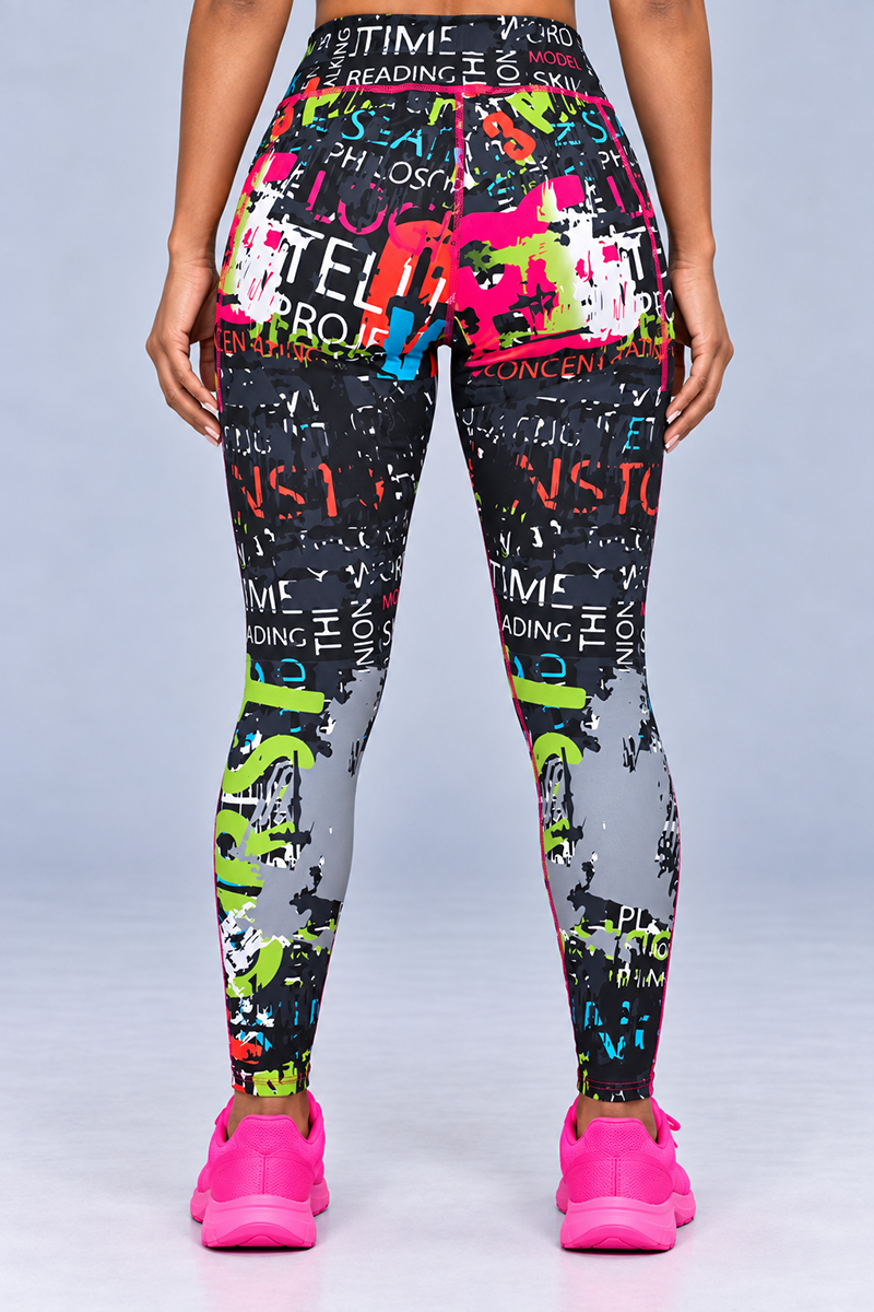 A person stands facing away, wearing the Electric Letters Tights—black stretchy leggings featuring colorful graffiti-style text and designs—paired with bright pink sneakers. The background is plain light gray, and their hands rest at their sides. These tights deliver a body-contouring fit for both comfort and style.