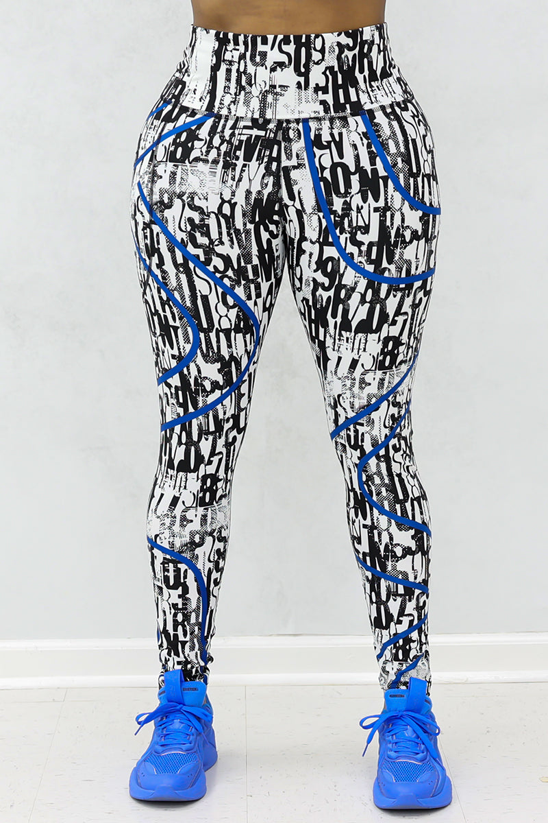 A person wears Blue Streak Tights in white-black-blue, featuring a graphic print with blue curved stripes, paired with bright blue athletic shoes, standing on a light-colored floor against a plain light background.
