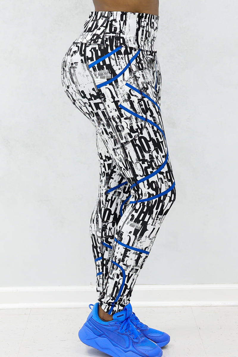 A person is shown from the waist down wearing Blue Streak Tights—high-waisted, black and white patterned leggings with blue accents and side pockets—paired with blue athletic shoes against a light gray background.