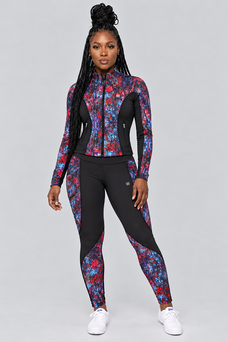 A woman stands facing forward, wearing the Kario Tights—a matching black athletic outfit adorned with blue, red, and purple geometric patterns. Made from a polyester spandex blend for optimal comfort and flexibility, the body-contouring Kario Tights feature 4-way stretch that moves seamlessly with her. She completes the look with white sneakers and long braided hair against a plain light gray background.