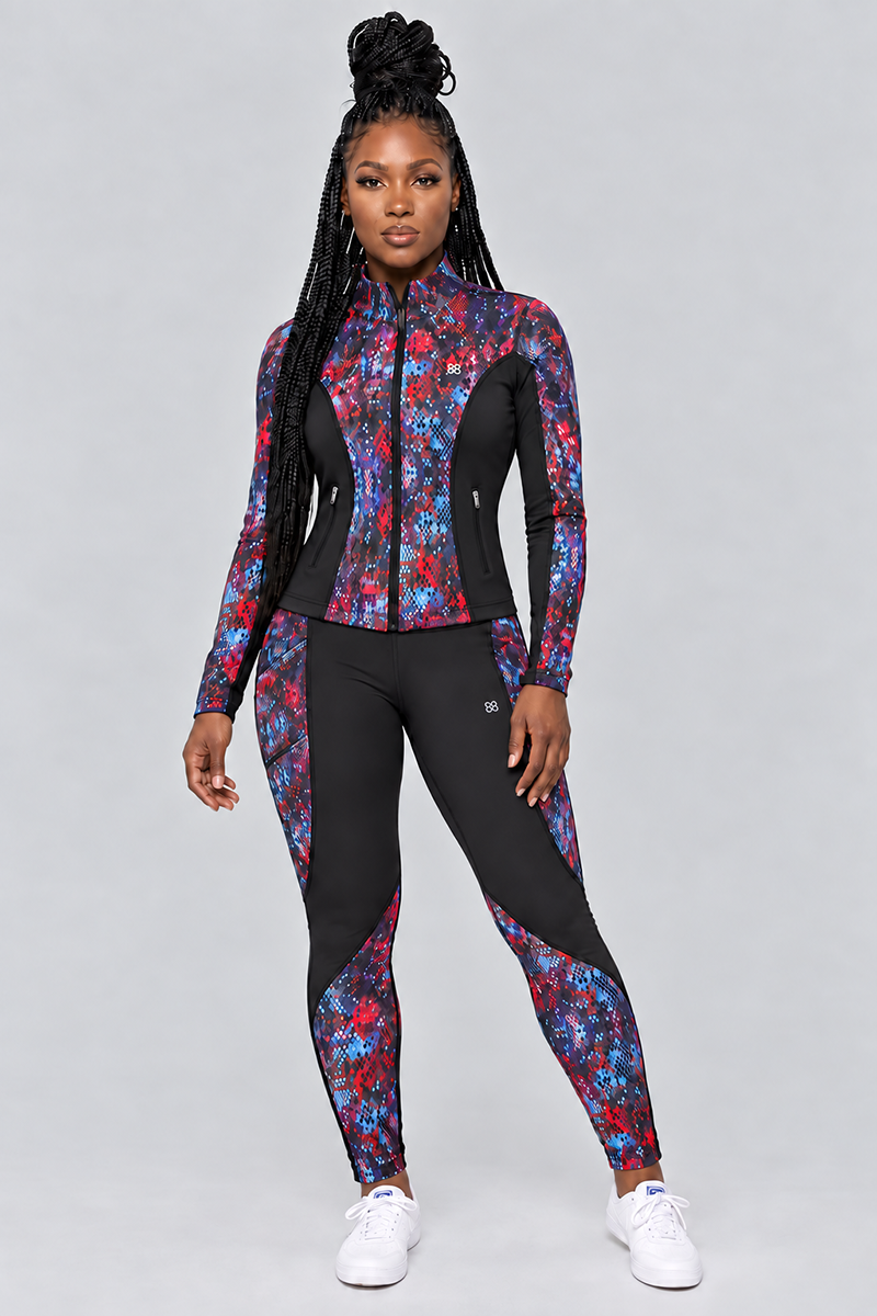 A woman stands facing forward, wearing the Kario Tights—fitted athletic leggings with a colorful geometric pattern and black panels. Crafted from polyester-spandex, the Kario Tights provide a body-contouring fit and 4-way stretch for optimal comfort and flexibility. She pairs them with white sneakers against a plain gray background.