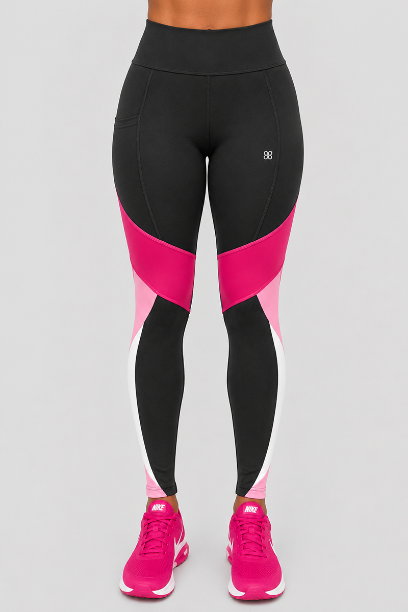 A person is seen from the waist down wearing Velocity Tights—high-waisted black leggings featuring pink and white color block accents, crafted with a body-contouring fit and 4-way stretch for maximum comfort. The look is completed with bright pink Nike sneakers, and the individual stands against a plain light gray background, with their torso out of view.