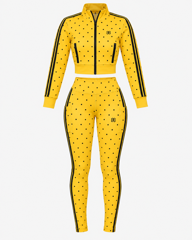 The Spotlight Jacket (SAMPLE SALE)—a yellow two-piece athletic outfit featuring black polka dots, black stripes on the sleeves and legs, a front zipper jacket, and matching high-waisted leggings—is displayed on a white background and available now at a discounted price.