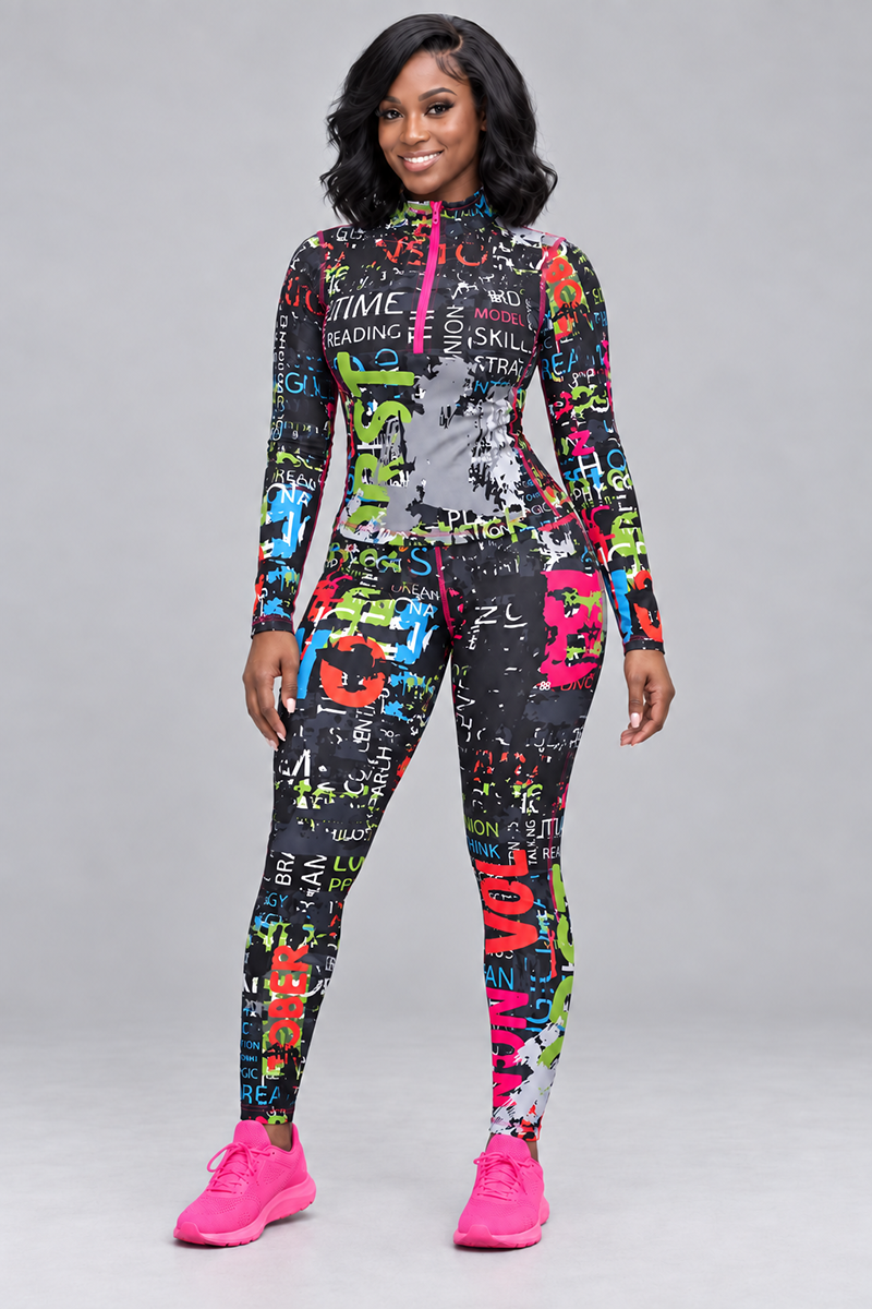 Wearing the Electric Letters Half-Zip Pullover, a woman stands smiling on a plain gray backdrop. The colorful, long-sleeve top features various words and abstract patterns on stretchy polyester spandex for comfort, and she pairs it with bright pink sneakers as she faces forward.