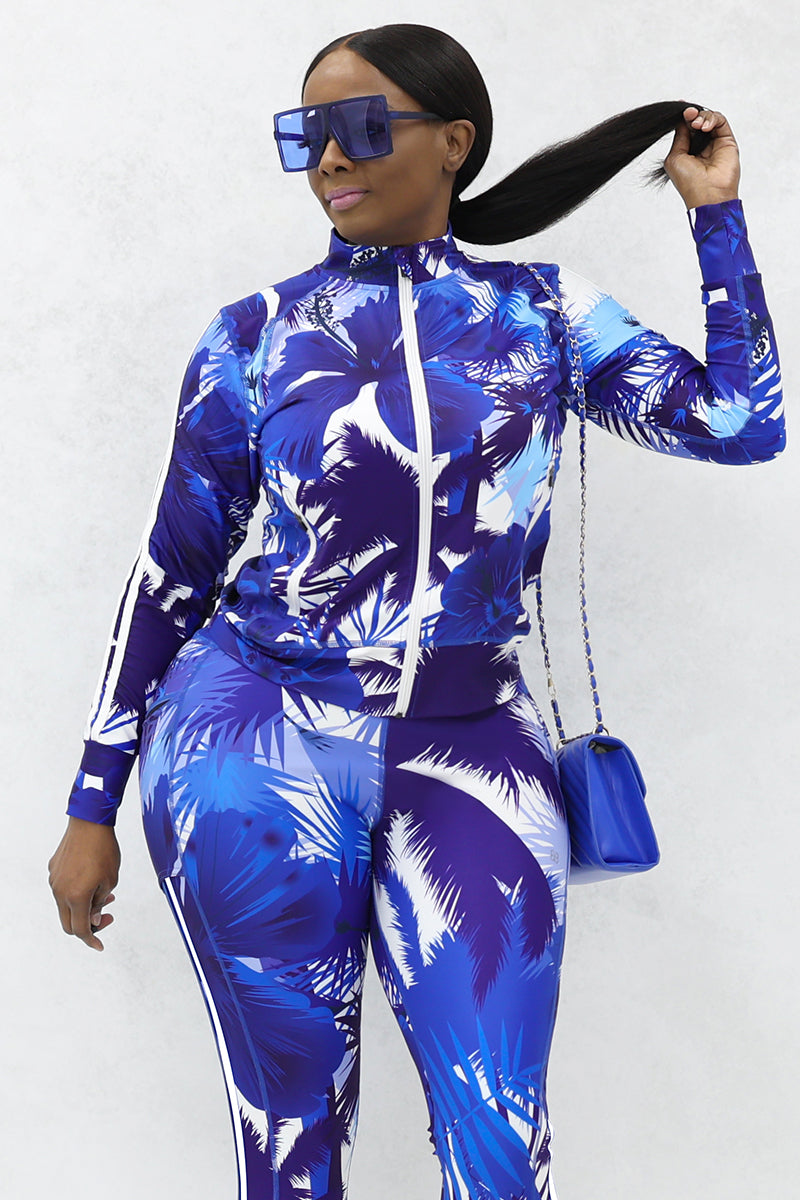 A woman wearing sunglasses, purse and long-sleeved zipper jacket with blue and white tropical print.