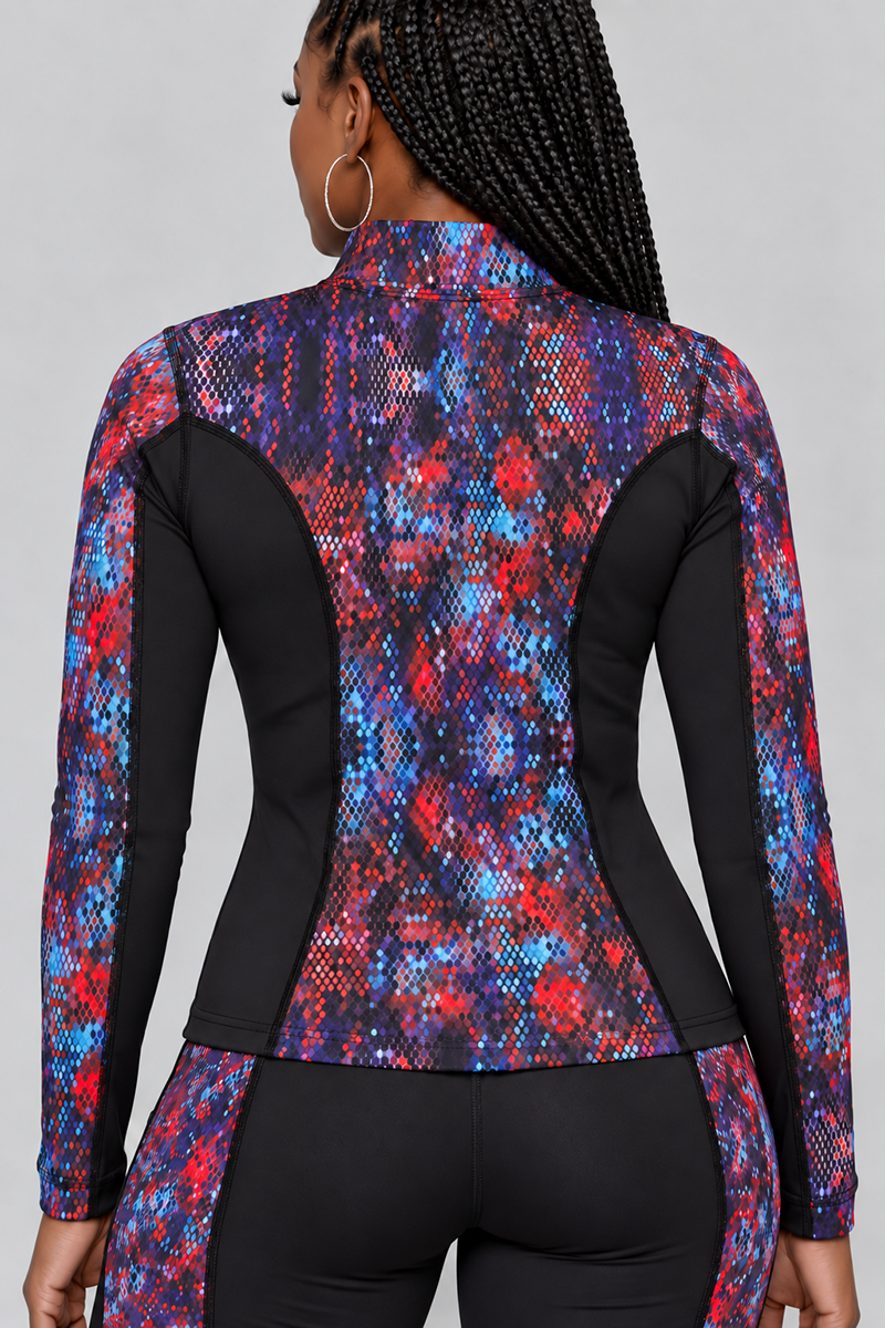 A woman with braided hair is shown from the back wearing the Kario Jacket—a fitted, long-sleeve athletic top paired with matching pants in a red, blue, and black patterned design. The outfit features a body-contouring fit that moves with her, thanks to its 4-way stretch fabric. The background is plain and light gray.