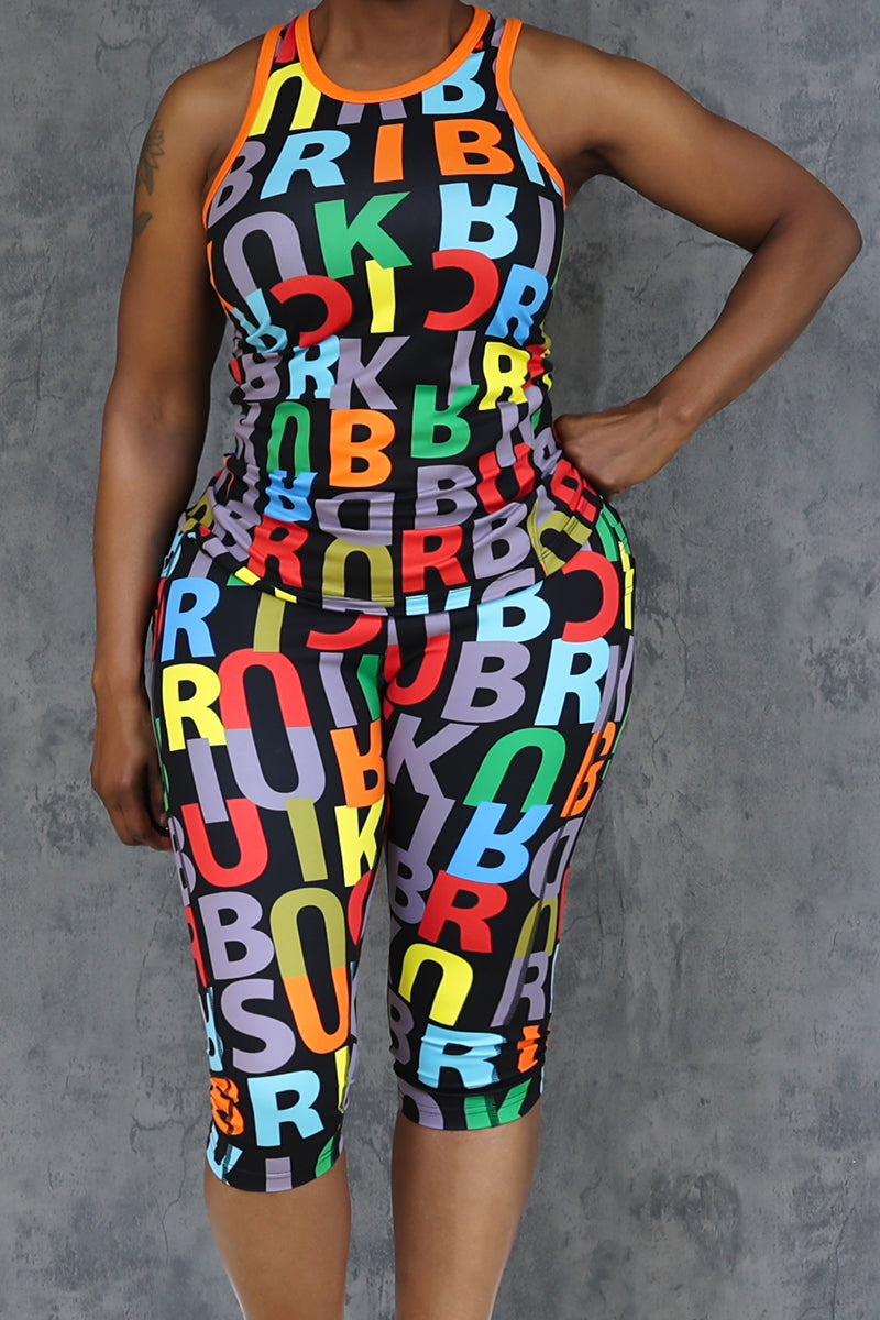Against a gray textured background, a person wears the Brick Built Lingo Pop Tank in Multi and matching capris, both featuring a vibrant overlapping letter print.