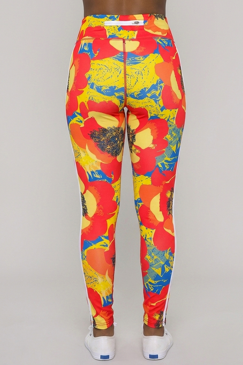 A person wearing the Orange Crush Tights—high-waisted, brightly colored 4-way stretch leggings featuring a bold red, yellow, and blue floral pattern—is shown from the back against a plain background.