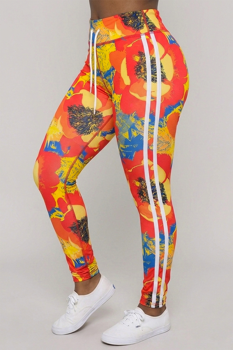 A person wearing the Orange Crush Tights—multi-color, bright floral-print 4-way stretch leggings featuring red, yellow, and blue hues with white vertical side stripes—paired with white sneakers and shown from waist to ankles against a plain background.