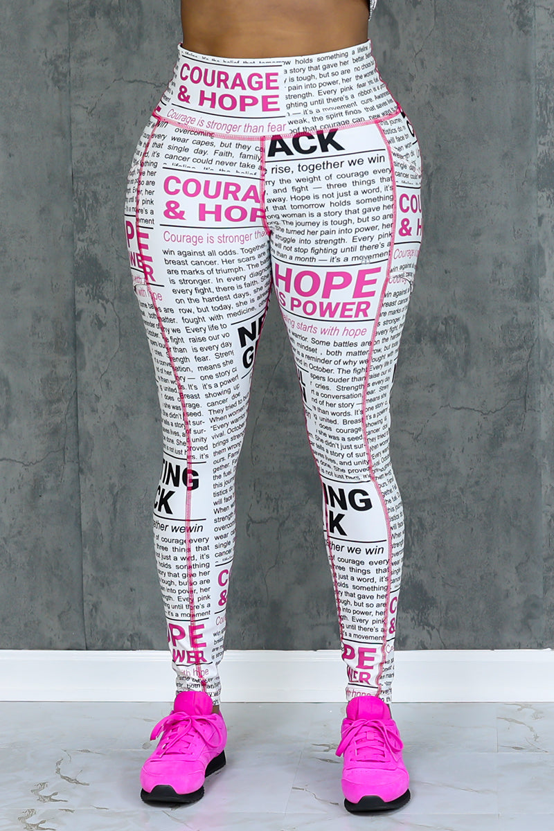 A person stands against a gray textured wall in Pink News Tights (White-Black-Pink), featuring high-waisted 4-way stretch compression fabric with bold black and pink phrases, paired with bright pink athletic shoes.