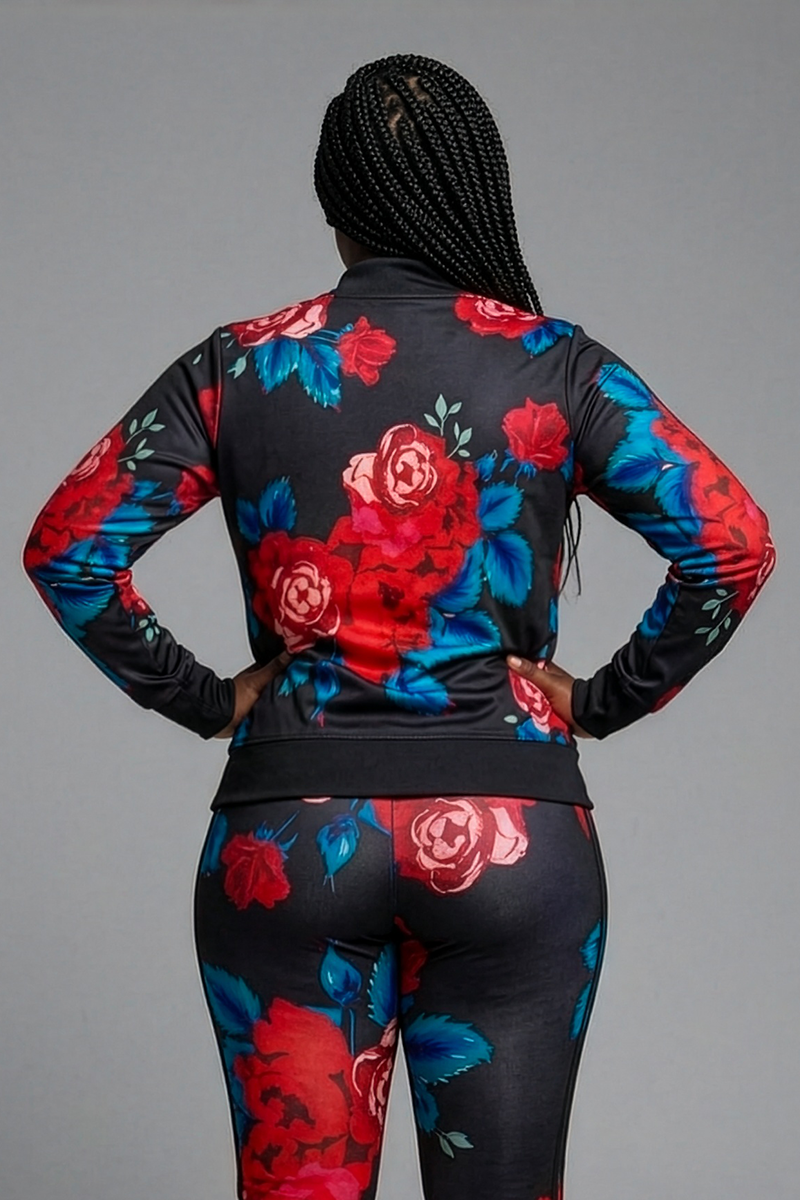 A person with long braids stands with their back to the camera, wearing the Red Roses Jacket—a black floral brushed fleece piece with bold red and blue flowers. The background is plain gray.