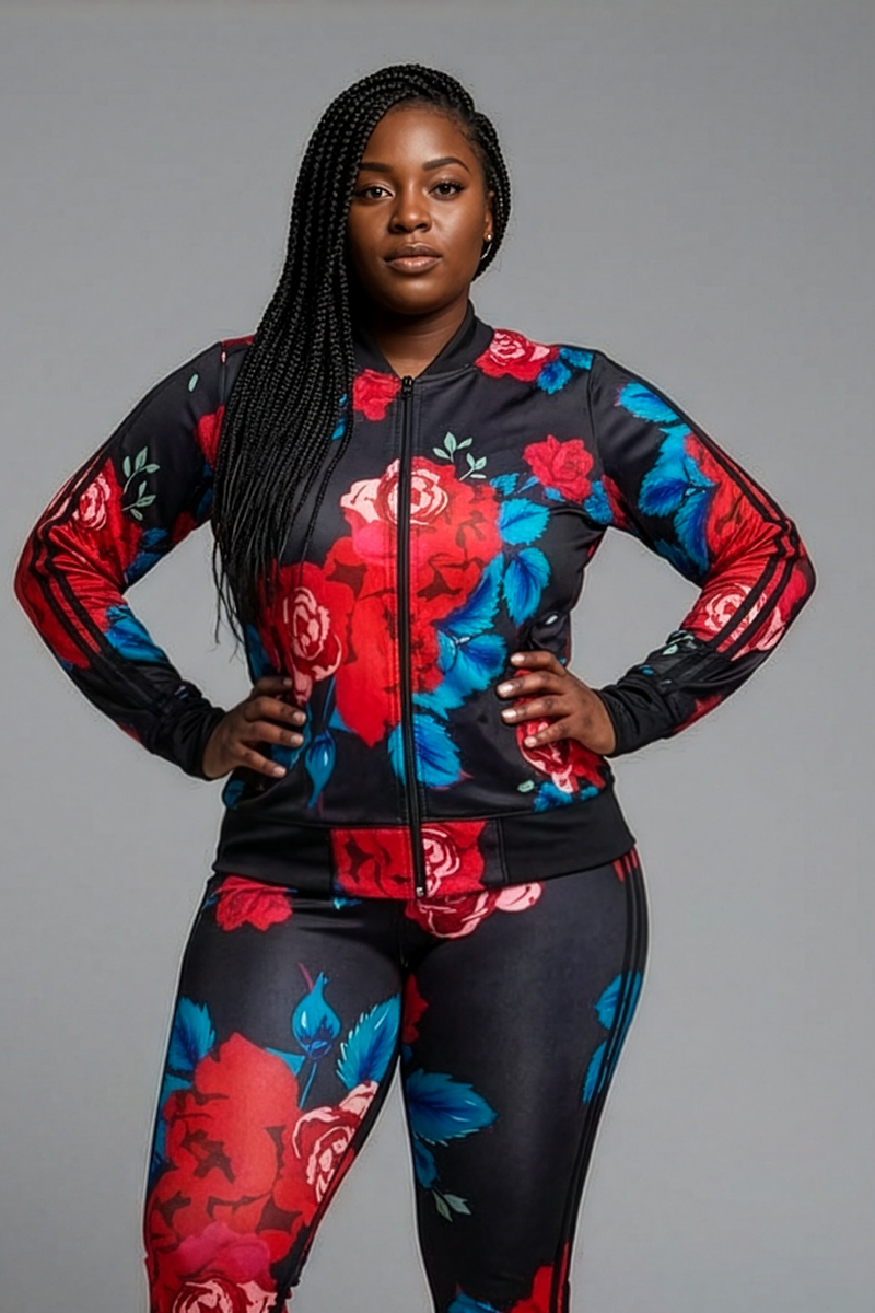 A woman with long braids and a neutral expression faces forward, wearing the Red Roses Jacket in Black-Red with large floral prints and zippered pockets. She pairs it with matching pants against a plain gray background.
