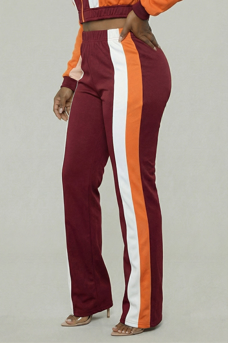 A person wears Color Block SweatPants in burgundy, orange, and cream with an elastic waistband, flared hem, and standout orange and white side stripes, styled with a matching jacket and open-toe heels.