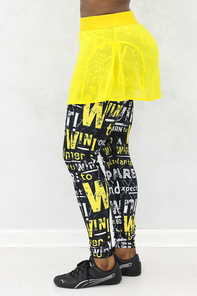 A woman wearing a yellow mesh tennis skirt with printed black tights. The skirt features a stretchy material and a drawstring waist for comfort and style.