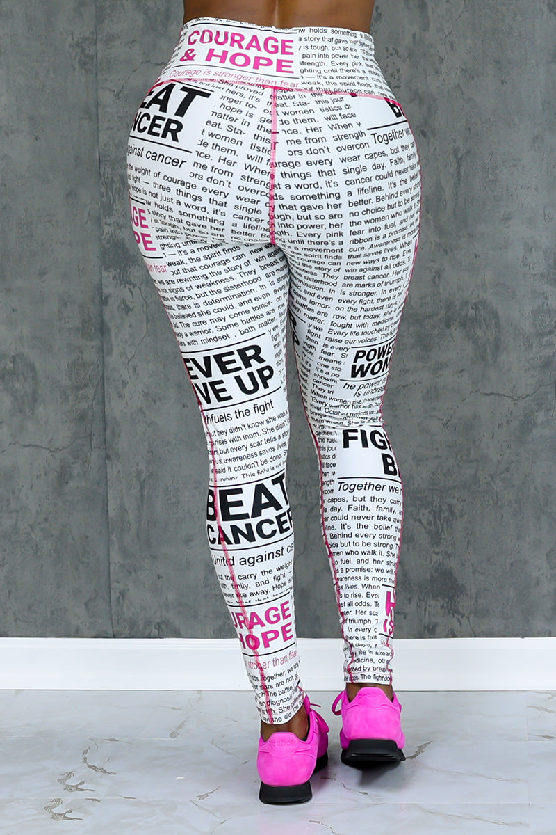 A person faces away from the camera wearing Pink News Tights featuring black and pink motivational cancer text, paired with bright pink athletic shoes, set against a gray textured wall and white floor.