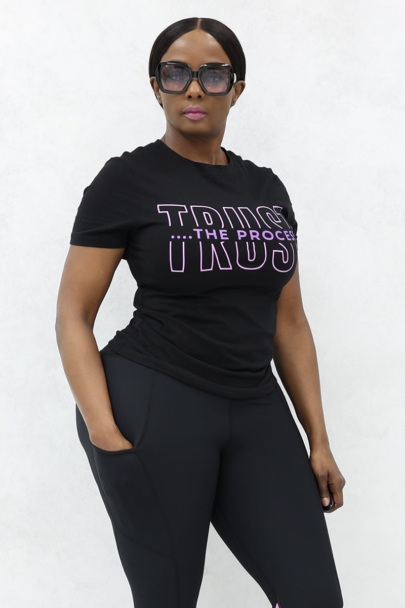 A girl wearing black glasses and a half-sleeve T-shirt with the text "Trust the Process" written on it.