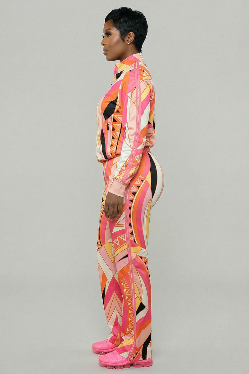 A person stands in profile against a plain background, wearing Vanta Pants—a colorful, relaxed-fit tracksuit bottom with abstract pink, orange, and yellow patterns, an elastic waistband, and matching pink sneakers.