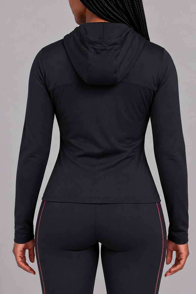 A person stands facing away from the camera, wearing the Velocity Jacket—a fitted black polyester spandex jacket with flatlock seams—and black leggings featuring pink stripes on the sides. The background is plain and light gray.