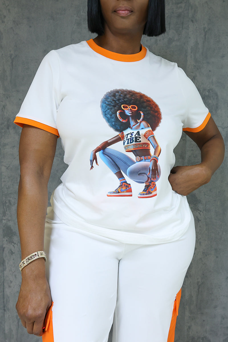 A woman stands against a gray background wearing the Vibe Short Sleeve T-Shirt in Orange-White, featuring a graphic of an African American woman with an afro, sunglasses, hoop earrings, and sneakers.
