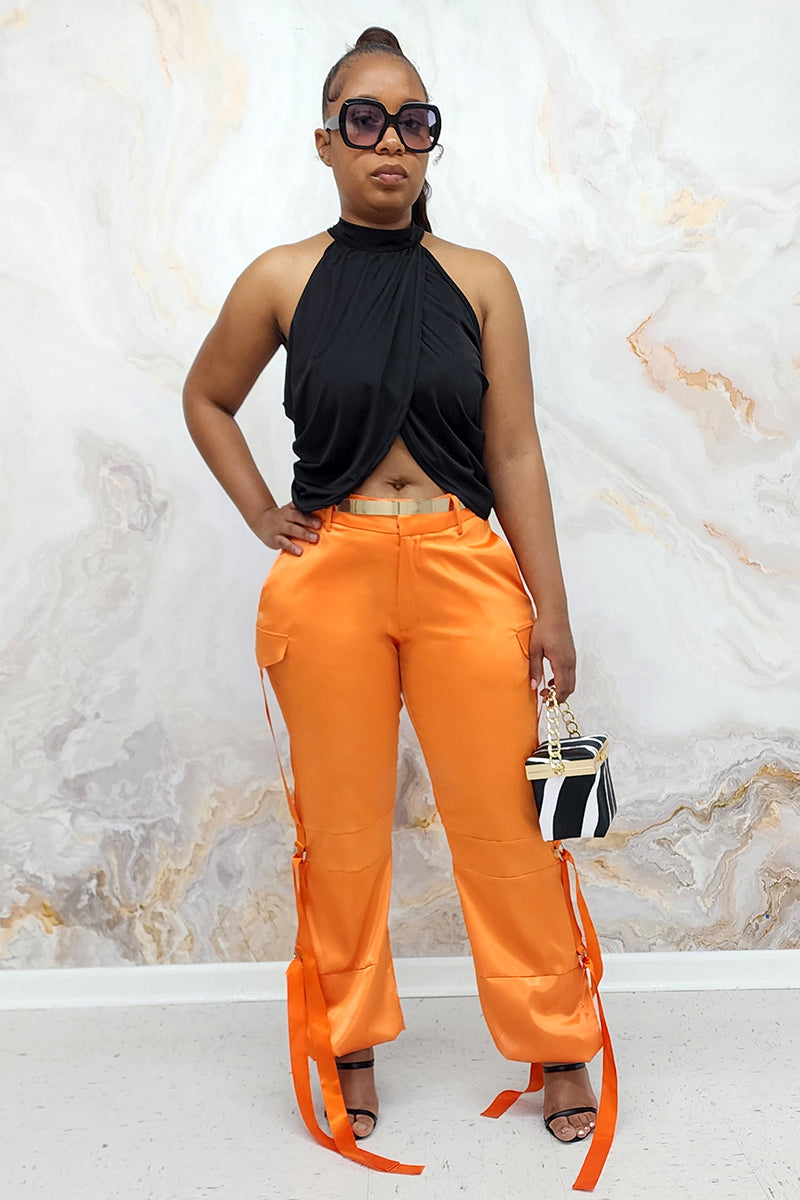 A woman wearing Orange Utility Pants made of smooth satin fabric, featuring a cinched ankle and tie straps for a trendy, functional look.