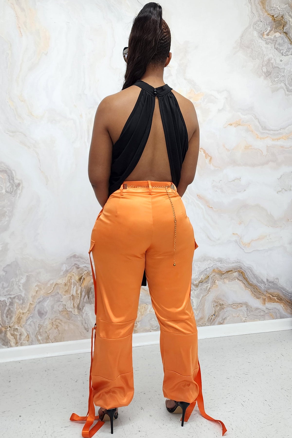 A woman wearing Orange Utility Pants made of smooth satin fabric, featuring a cinched ankle and tie straps for a trendy, functional look.