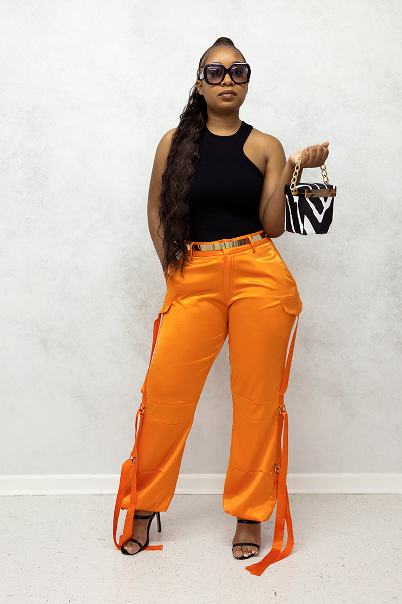 A woman wearing Orange Utility Pants made of smooth satin fabric, featuring a cinched ankle and tie straps for a trendy, functional look.