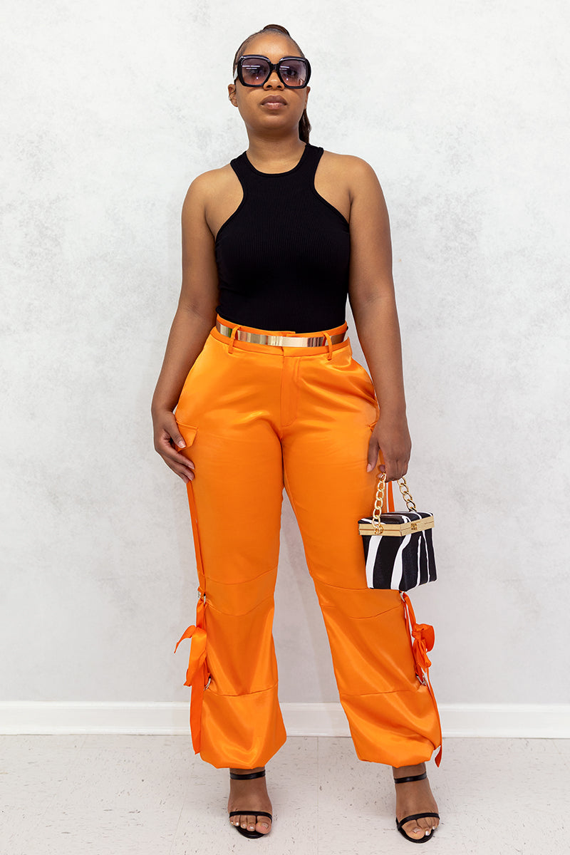 A woman wearing Orange Utility Pants made of smooth satin fabric, featuring a cinched ankle and tie straps for a trendy, functional look.