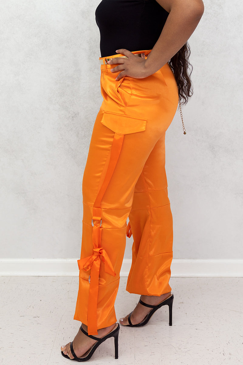 A woman wearing Orange Utility Pants made of smooth satin fabric, featuring a cinched ankle and tie straps for a trendy, functional look.